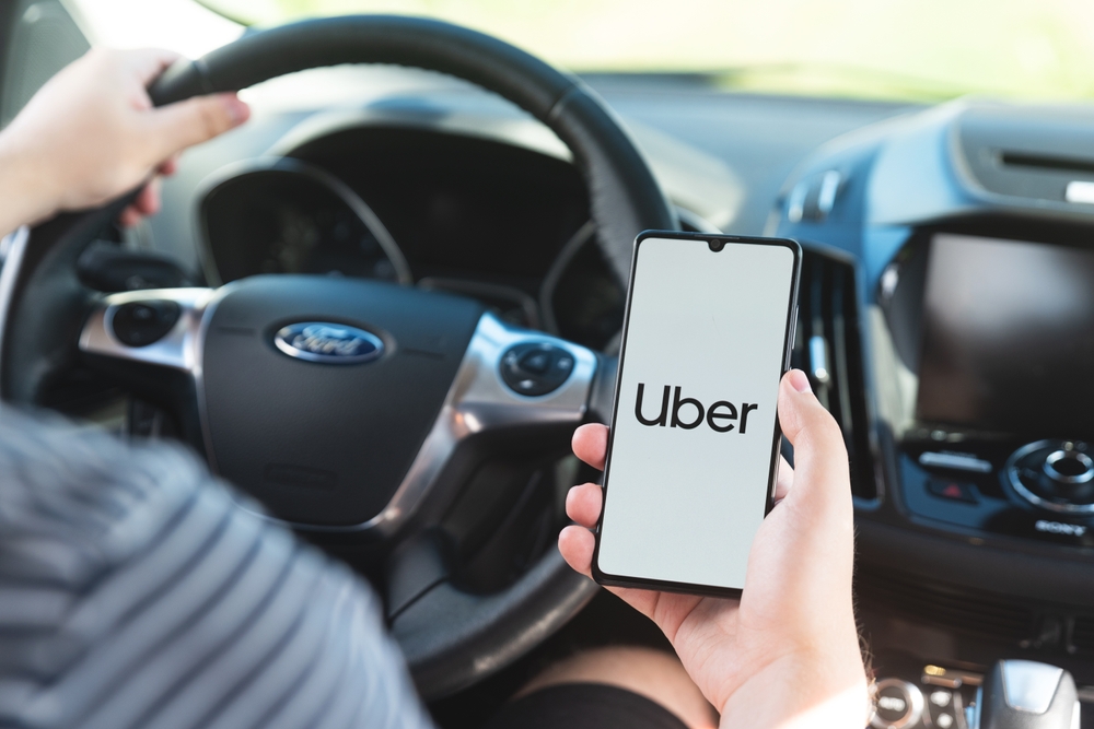 Close-up of driver using cell phone with Uber logo on screen